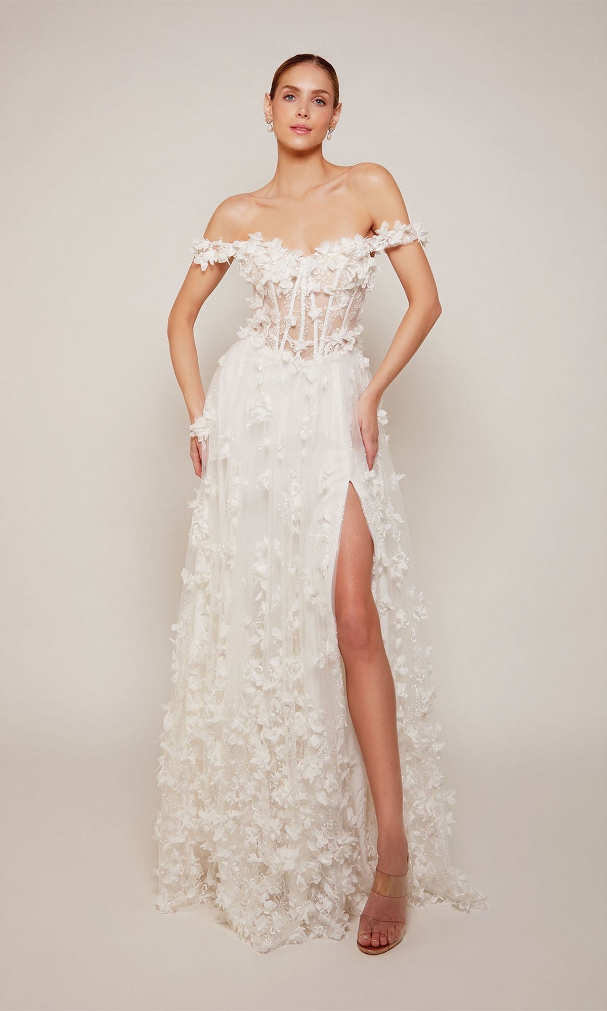 A woman poses in the Alyce 61308 off-shoulder long floral dress in diamond white, featuring floral appliqué accents and a high slit, set against a plain background.